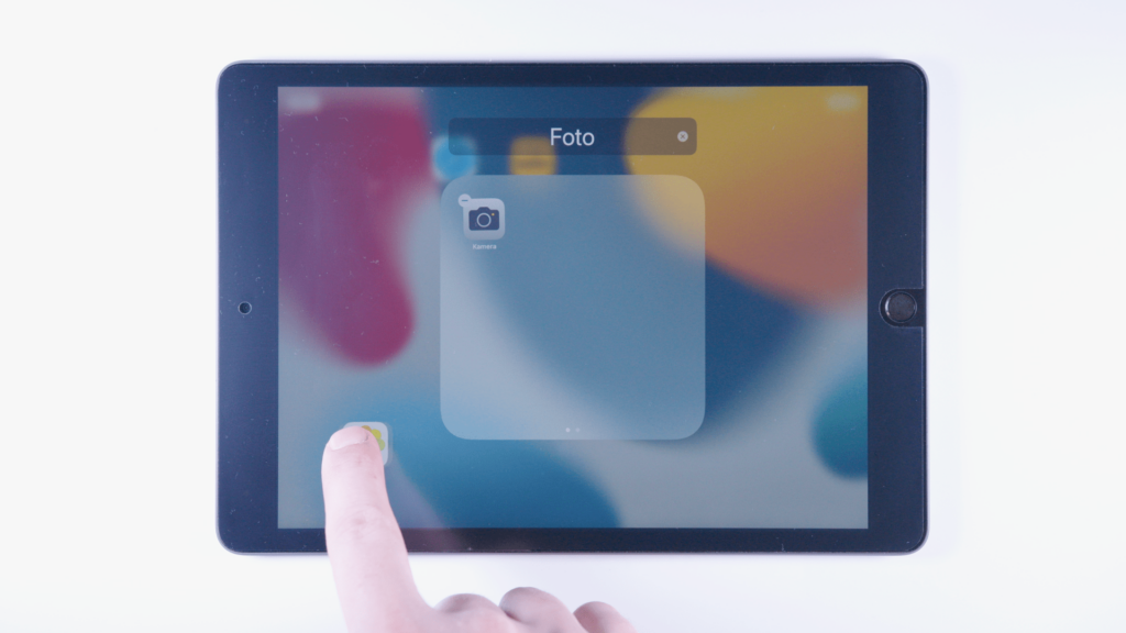iPad: Ein Finger tippt auf eine App und zieht sie aus einem Ordner.