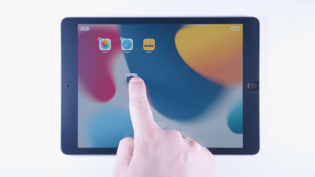 iPad: Ein Finger tippt auf eine App und zieht sie nach links.