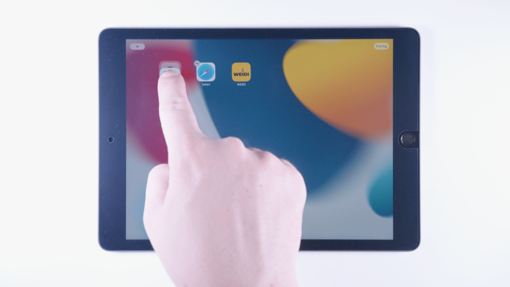 iPad: Ein Finger tippt auf eine App und zieht sie auf eine andere App.