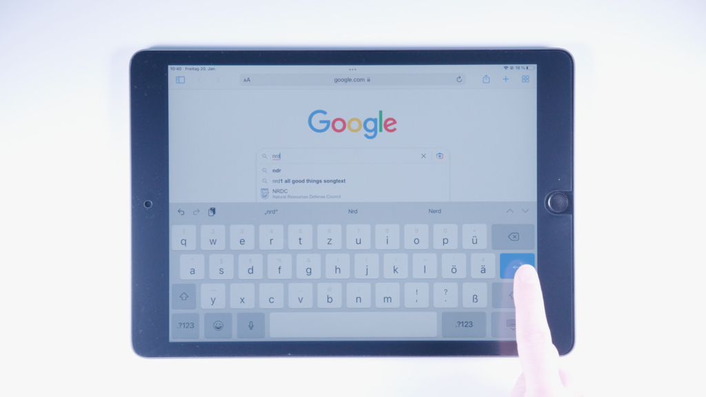 Ein iPad: Google-Suche: NRD ist eingetippt, Finger liegt auf der blauen Eingabetaste; Rechte, untere Bildschirmecke.