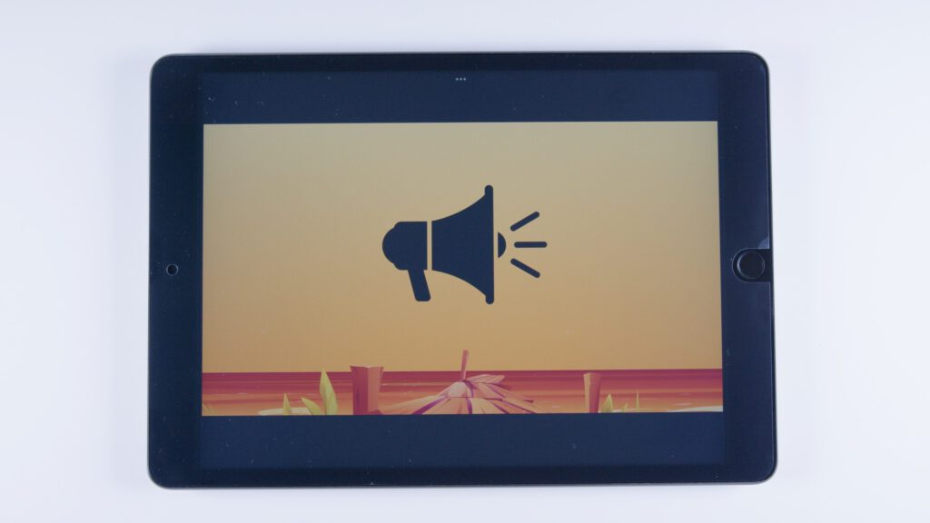 Tablet mit orangem Hintergrund. In der Mitte ein schwarzes Megafon-Symbol mit drei Schallwellen.