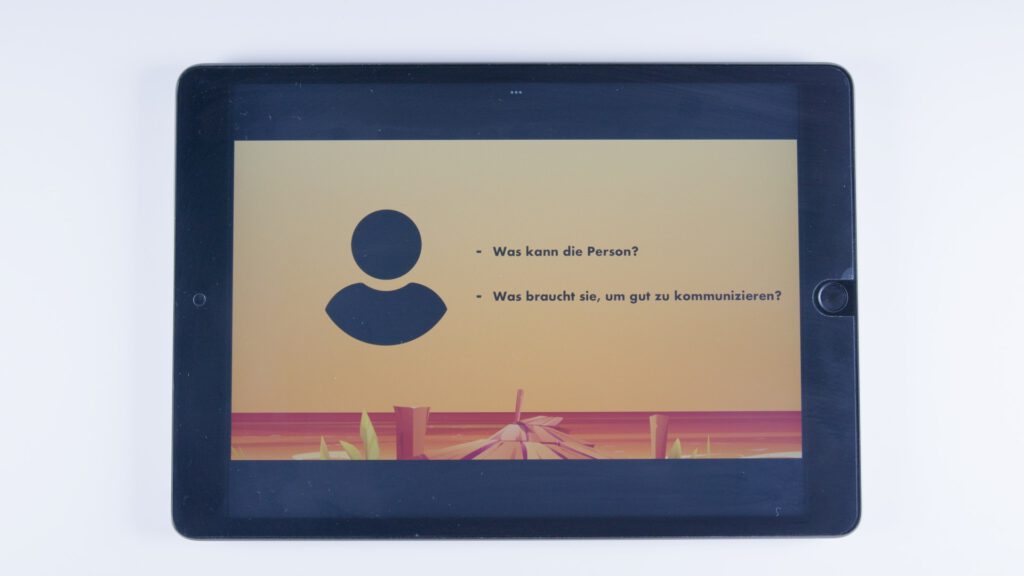 Ein Tablet zeigt auf orangem Hintergrund ein schwarzes Symbol einer Person. Daneben stehen die Fragen: „Was kann die Person?“ und „Was braucht sie, um gut zu kommunizieren?“.