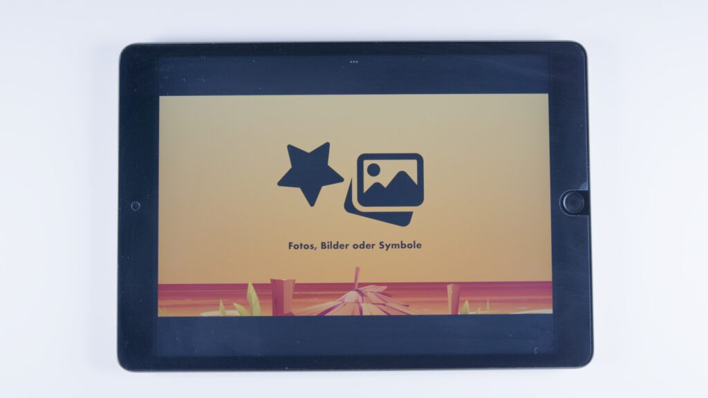Ein Tablet zeigt auf orangem Hintergrund zwei schwarze Symbole: ein Stern und ein Stapel Bilder mit einem Bergmotiv. Darunter steht: „Fotos, Bilder oder Symbole“.