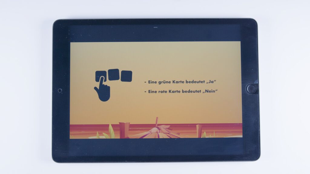 Tablet mit orangem Hintergrund. Links ein Symbol einer Hand, die auf Karten zeigt. Rechts steht: „Eine grüne Karte bedeutet ‚Ja‘ – Eine rote Karte bedeutet ‚Nein‘“.