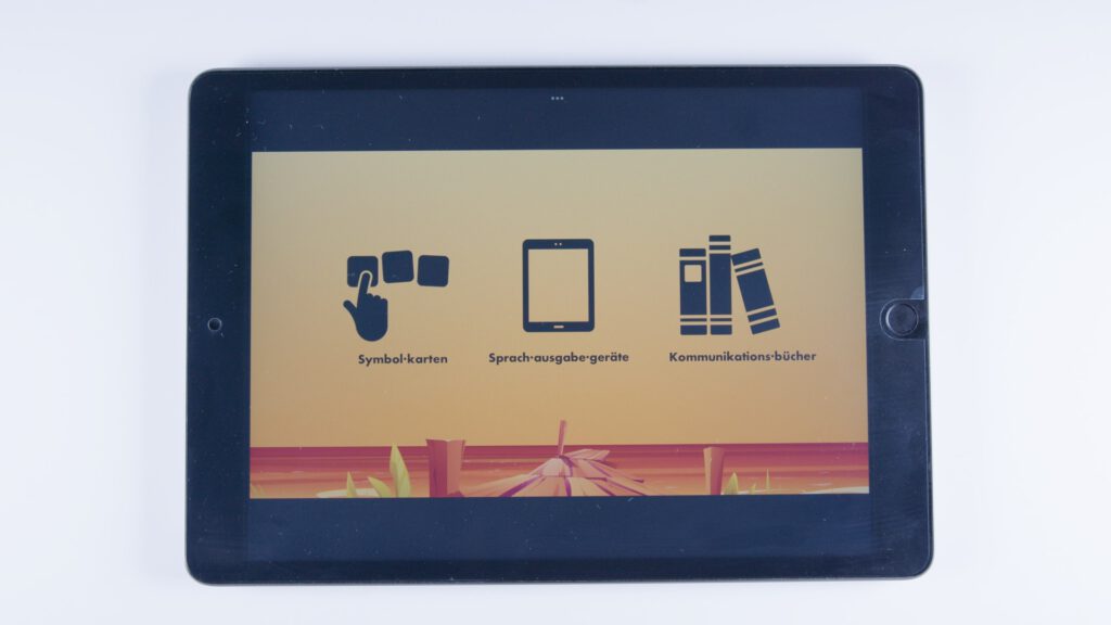 Tablet mit orangem Hintergrund. Drei Symbole: eine Hand mit Symbolkarten (beschriftet mit „Symbol·karten“), ein Tablet („Sprach·ausgabe·geräte“) und drei Bücher („Kommunikations·bücher“).