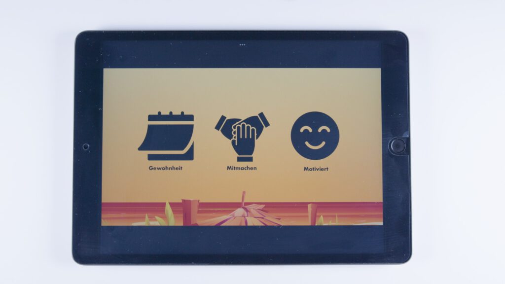 Tablet mit orangem Hintergrund. Drei Symbole: ein abgerissener Kalender mit dem Text „Gewohnheit“, zwei sich abklatschende Hände mit der Beschriftung „Mitmachen“ und ein lachendes Gesicht mit dem Text „Motiviert“.